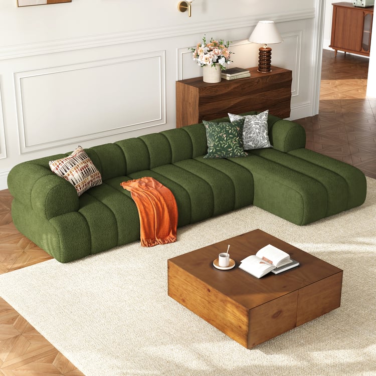 Green sectional sofa in a living room with a wooden coffee table and decorative items.