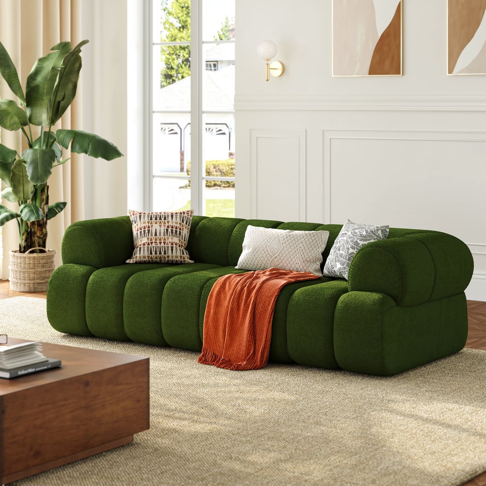 Green sofa with decorative pillows and a blanket in a living room setting.