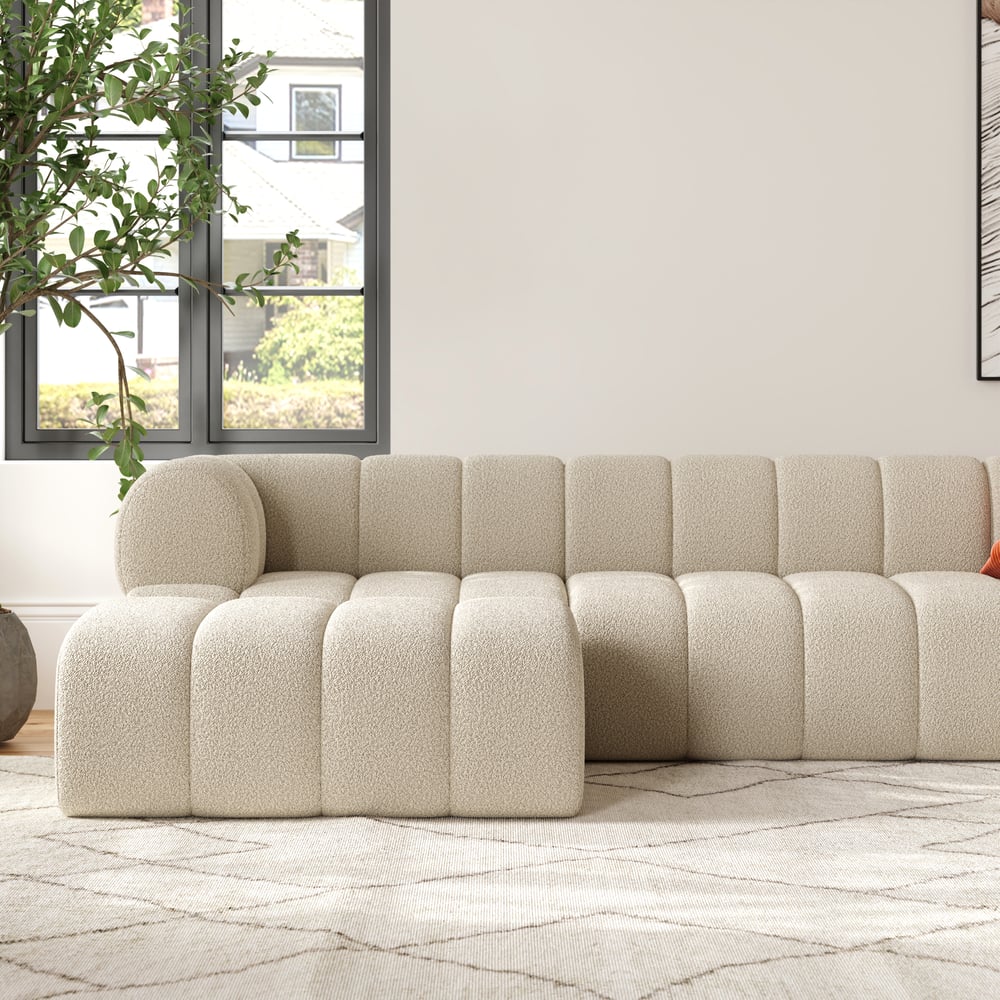 Beige sectional sofa in a living room with a plant and window in the background