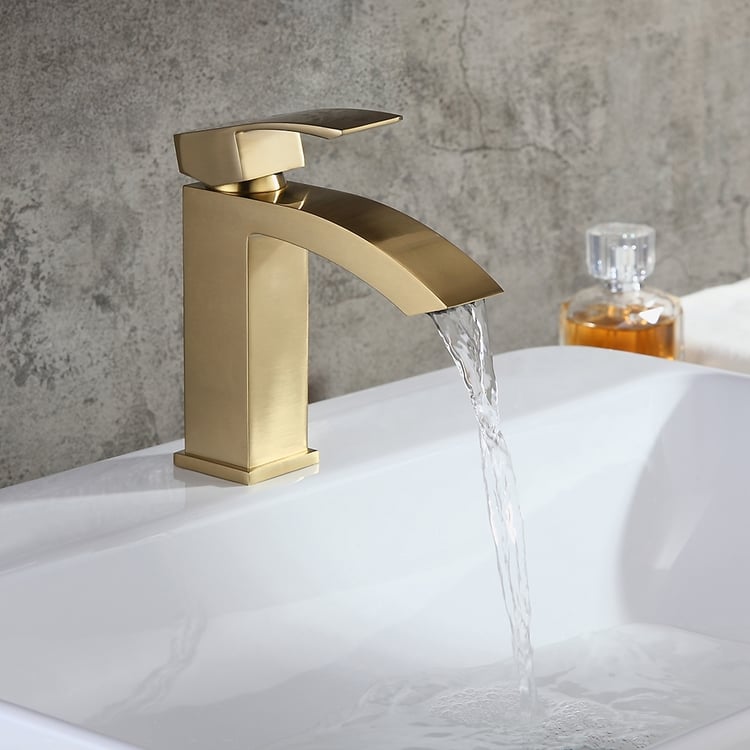 Gold faucet with water flowing into a sink against a gray stone wall.