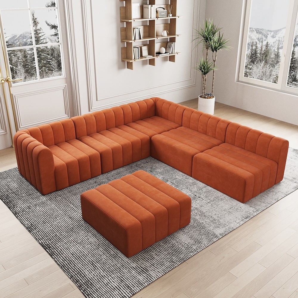 Orange sectional sofa with ottoman on a gray rug in a room with large windows and a bookshelf.