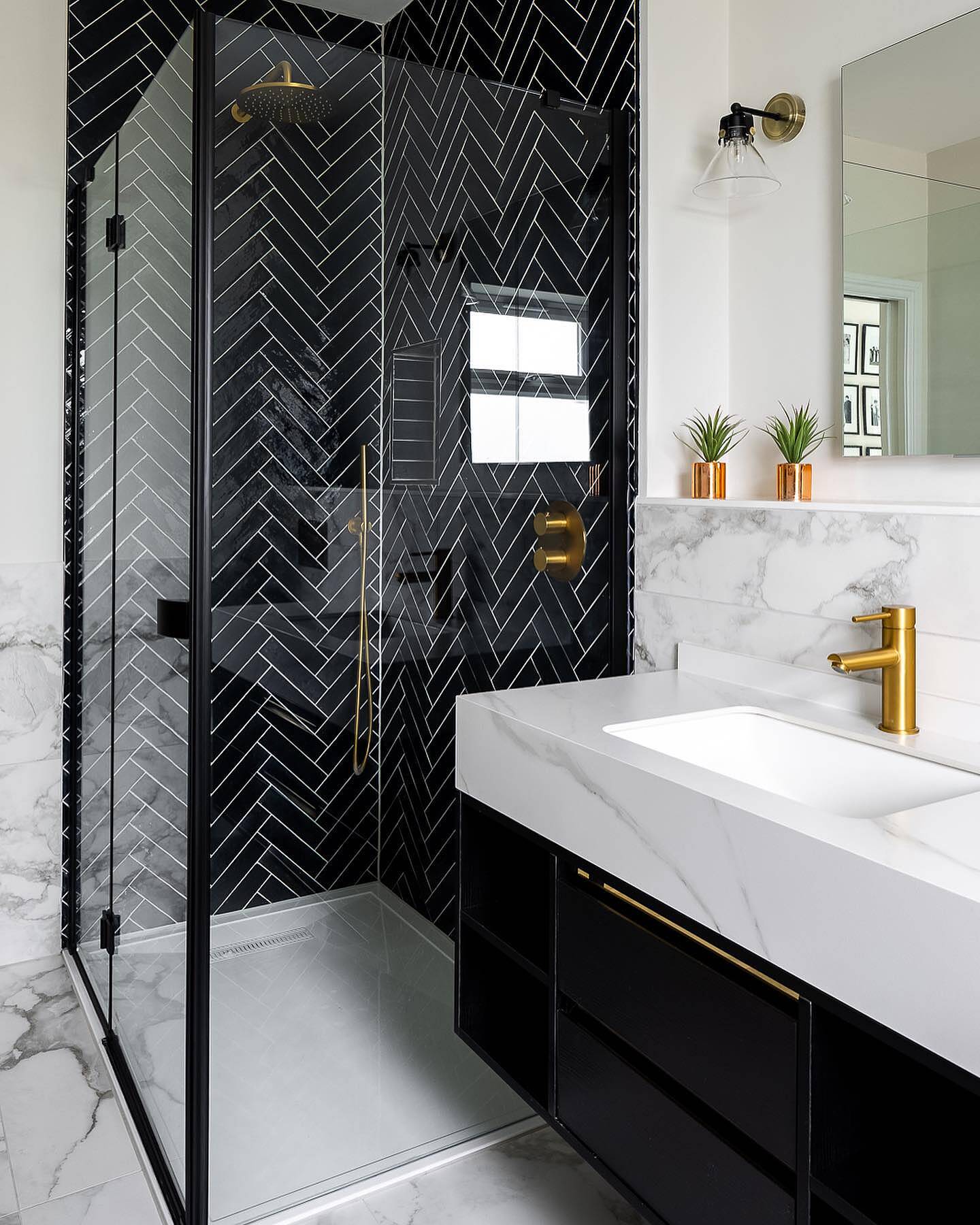 Modern bathroom with black shower enclosure, white countertop, and gold fixtures.