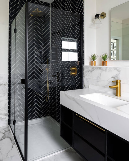 Modern bathroom with black shower enclosure, white countertop, and gold fixtures.