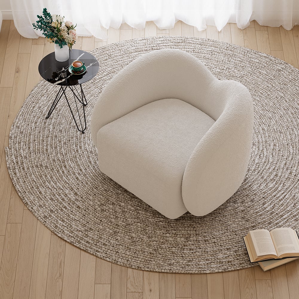 Round beige rug on a wooden floor with a modern chair and small table.