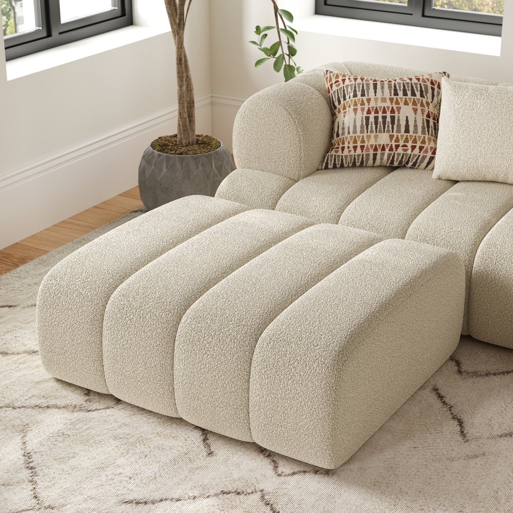 Beige sectional sofa with a patterned pillow in a room with a plant and window.