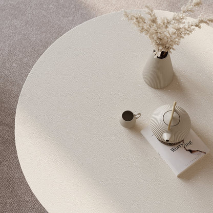 Round textured coffee table with a cup, vase, and book on a neutral background