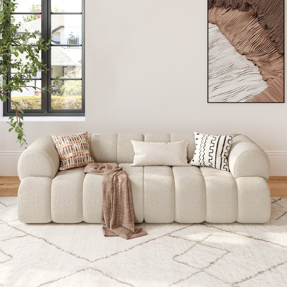 Beige sofa with decorative pillows and a blanket in a living room setting.