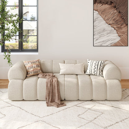 Beige sofa with decorative pillows and a blanket in a living room setting.