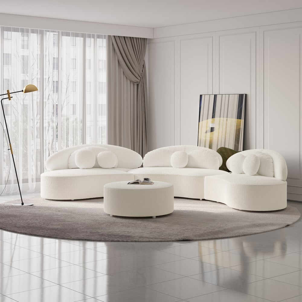 Modern white sofa set in a stylish living room with a round ottoman and decorative mirror.