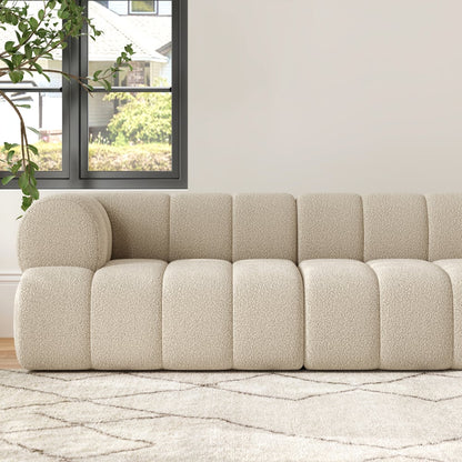 Beige sectional sofa in a living room with a window and plant in the background