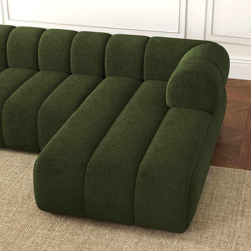 Green sectional sofa in a room with wooden flooring and white walls.