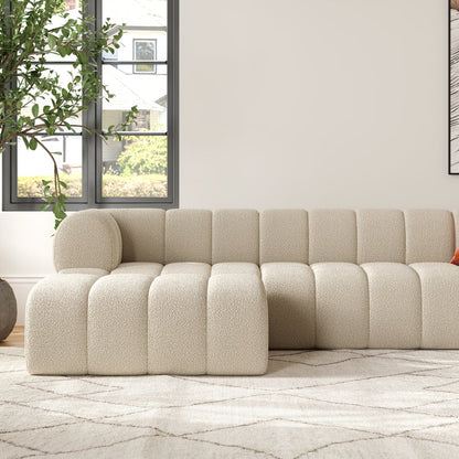 Beige sectional sofa in a living room with a plant and window in the background