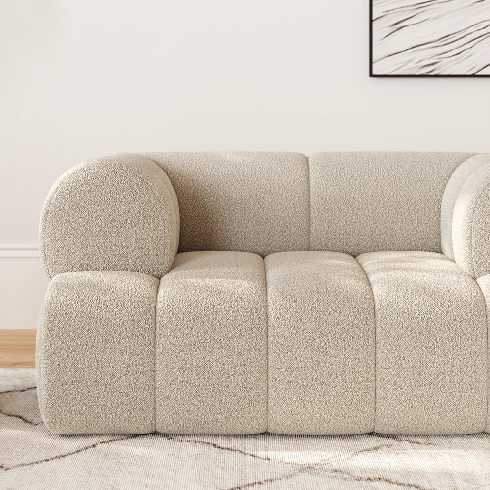 Beige textured sofa in a room with a light-colored wall and abstract art.