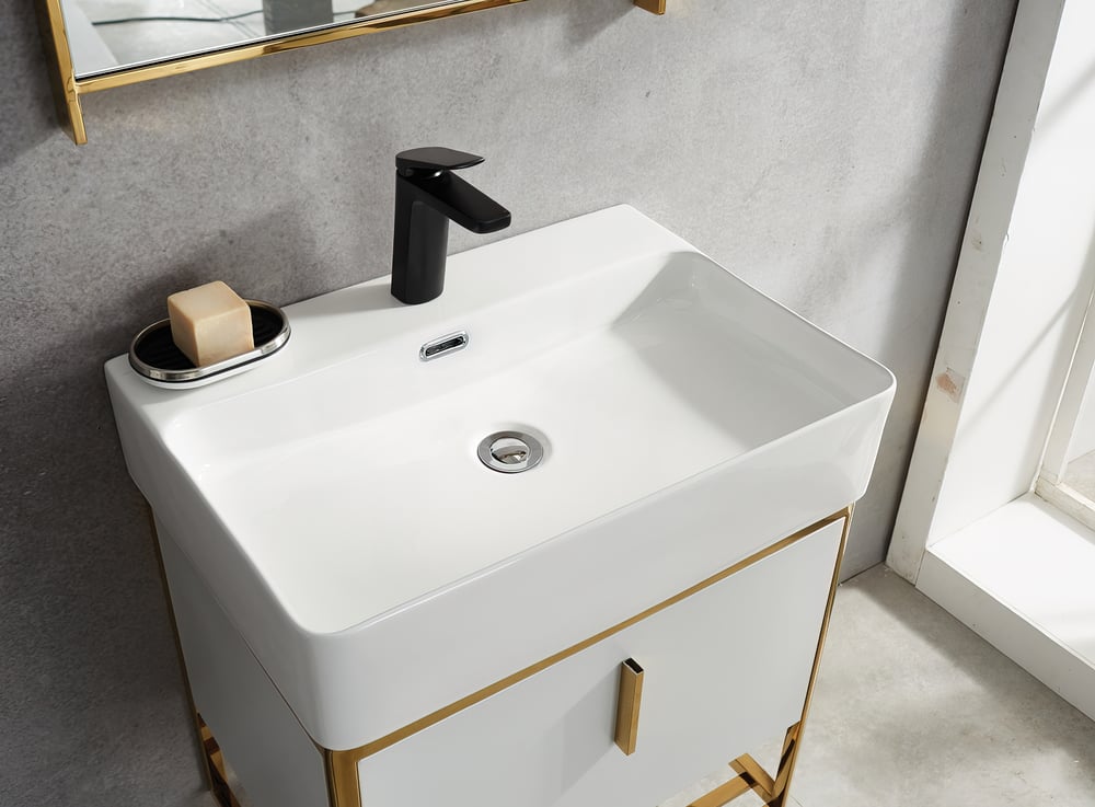 Bathroom vanity with white sink and gold accents, featuring a black faucet.
