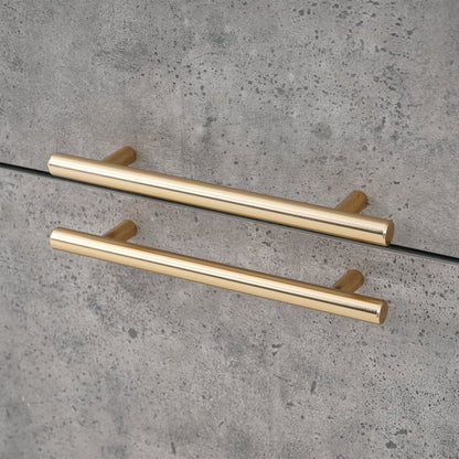 Two gold cabinet handles on a gray concrete surface
