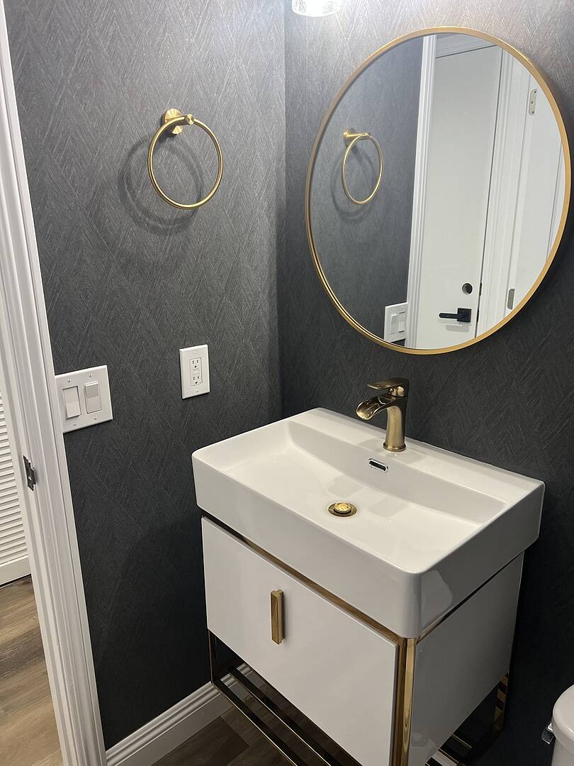 Bathroom vanity with white sink and gold fixtures against a gray wall.