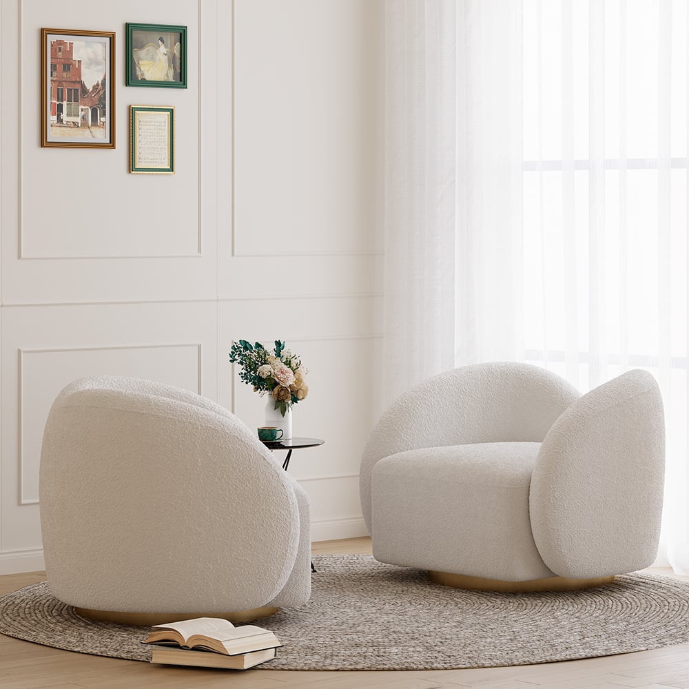 Two beige armchairs in a living room with a small table and books on a rug.